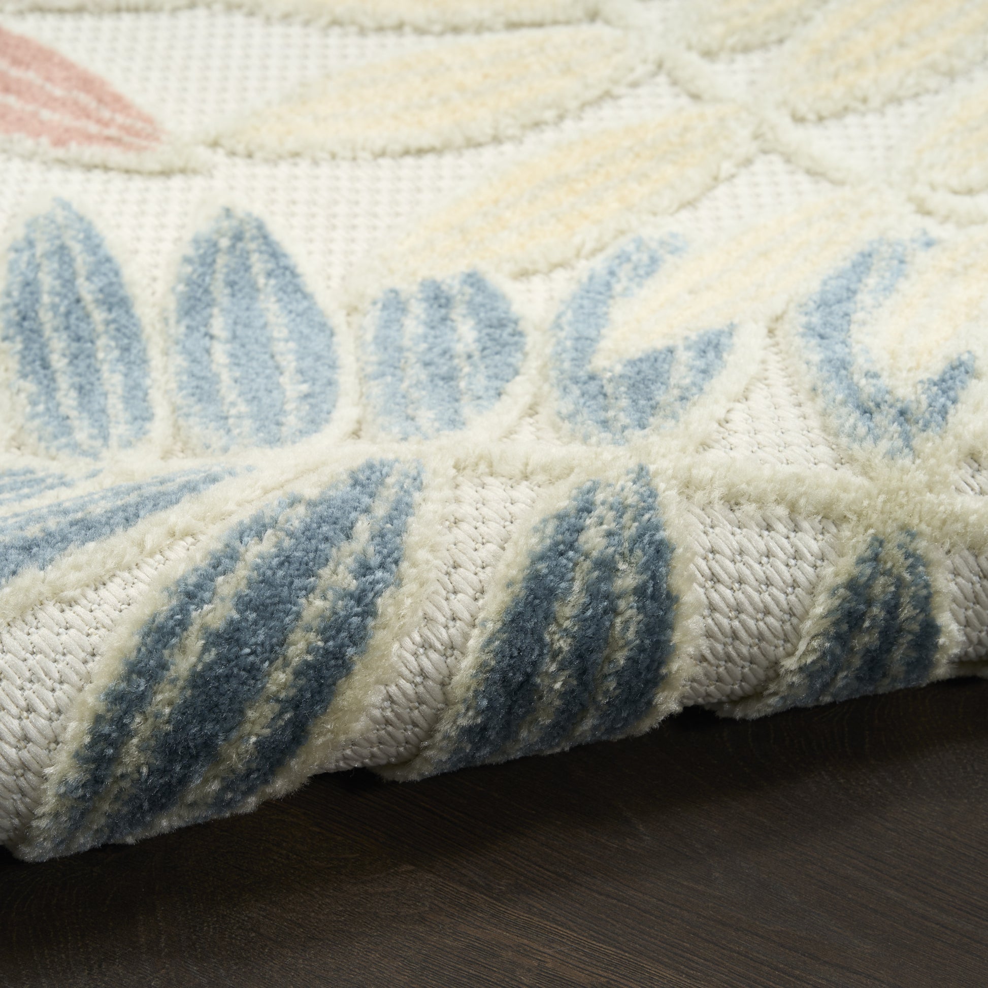 Cream and blue woven rug with leaf-like pattern, plush pile, folded edge on dark wood floor.