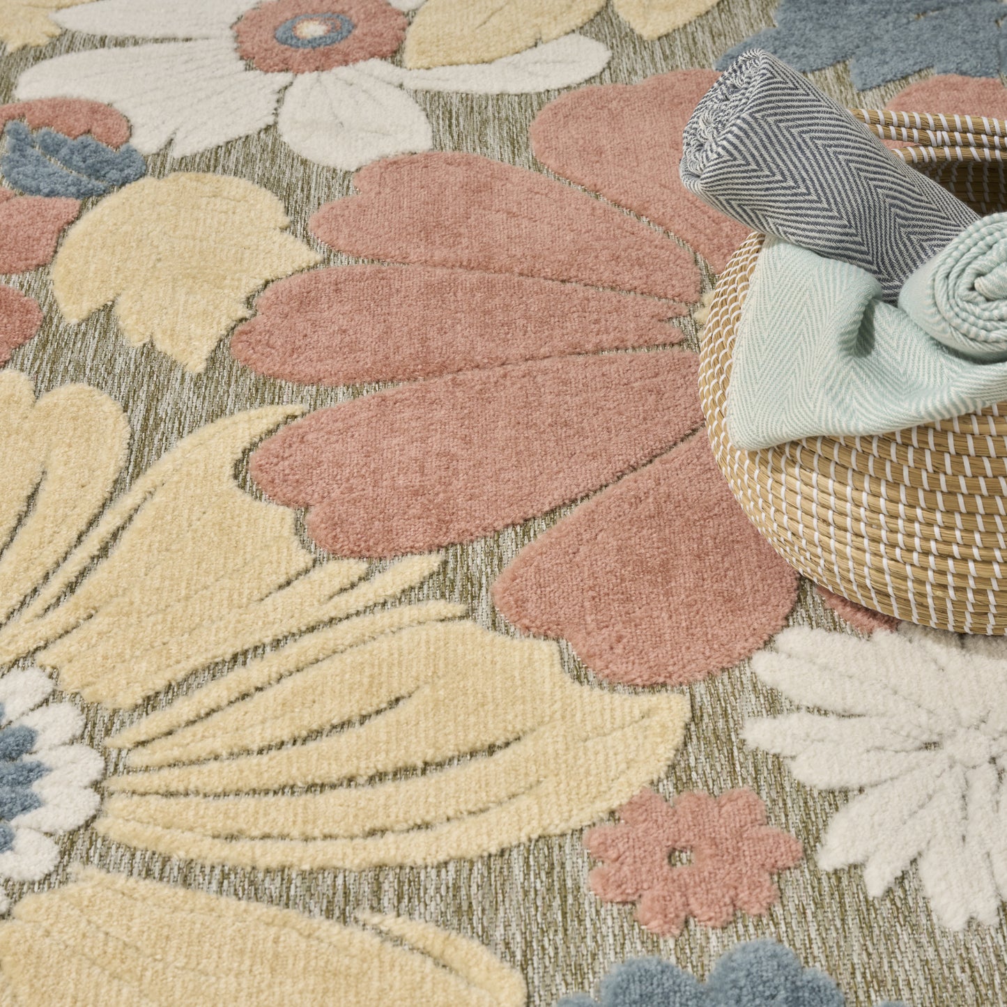Pastel floral area rug with oversized cream, pink, yellow petals; woven basket with folded mint and striped gray textiles