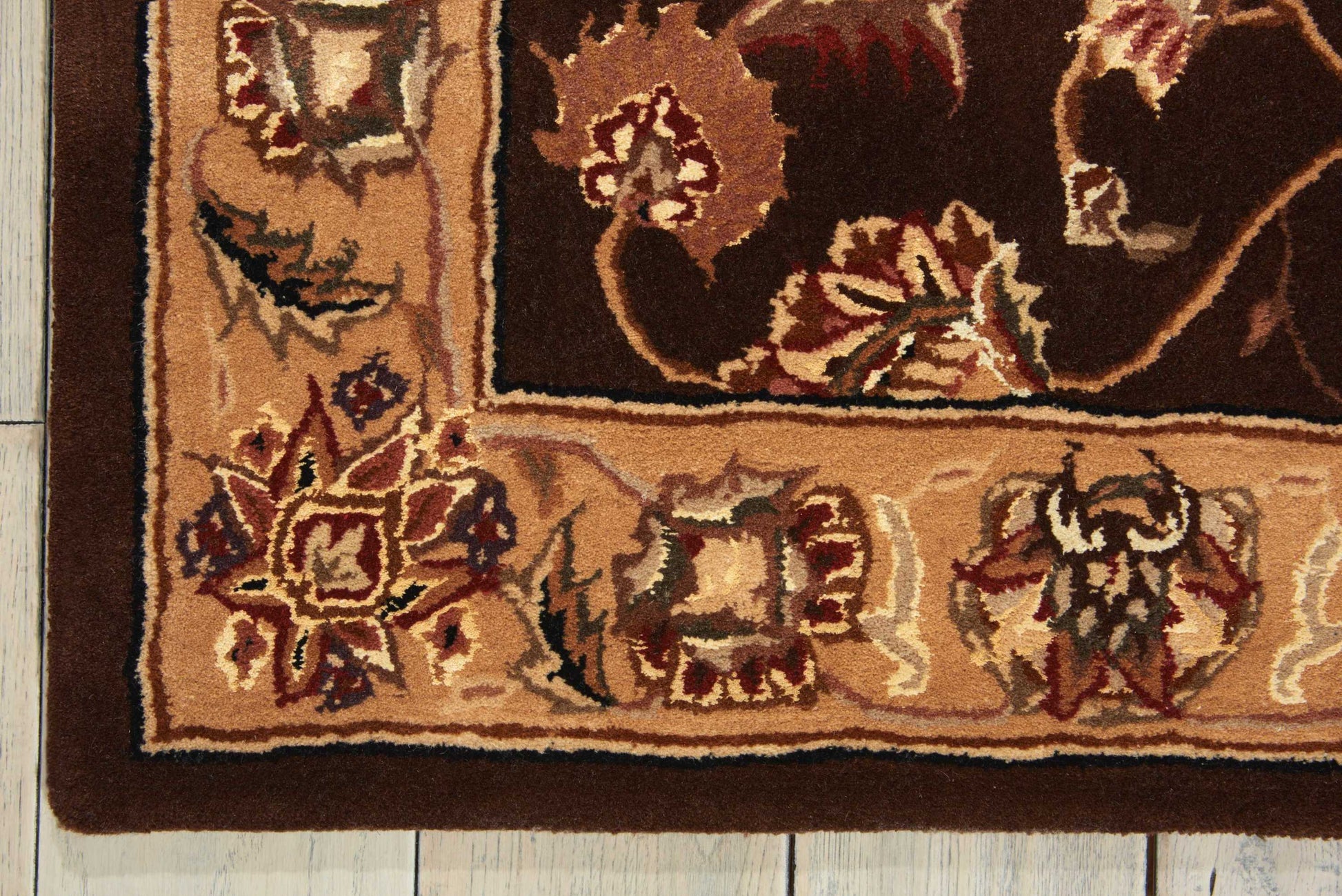 Corner view of brown oriental rug with a tan border and floral motifs on a wooden floor.