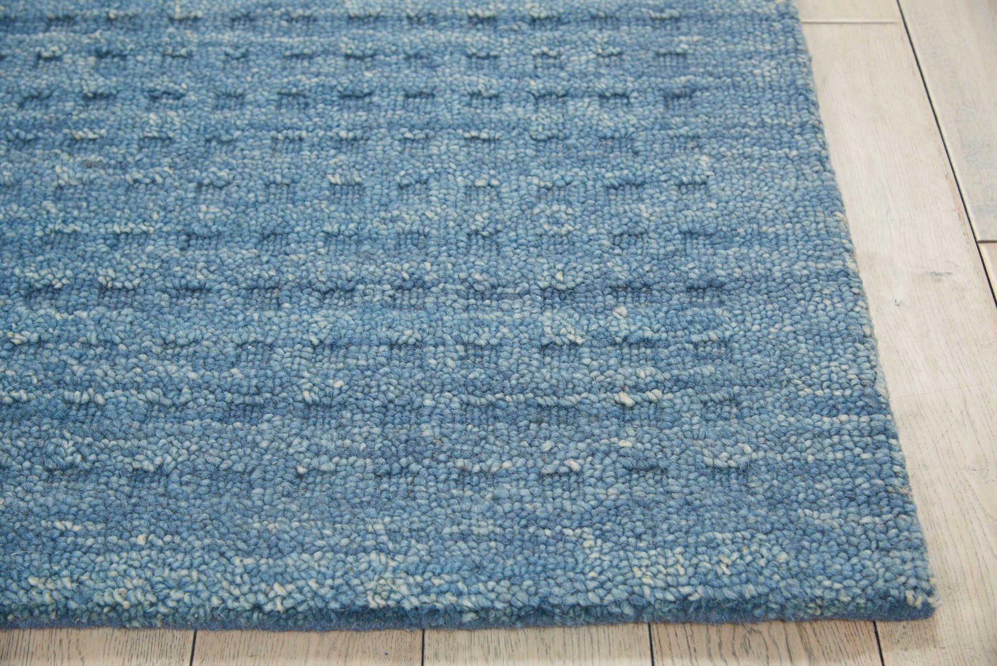 Blue textured loop-pile rug with cream flecks on a light wood floor.