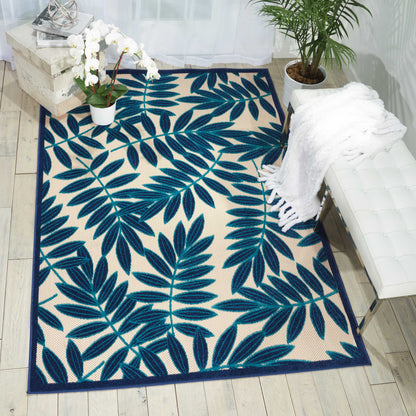Rectangular area rug featuring a bold blue tropical leaf pattern with a navy border on beige.