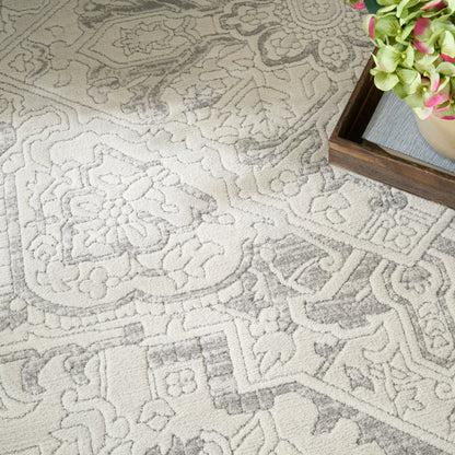 Neutral damask patterned area rug in cream and light gray; soft woven texture beside a wooden frame with green/pink flowers.