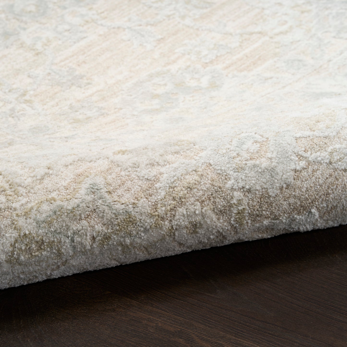 Cream & beige patterned plush area rug, rolled edge on dark wood floor.