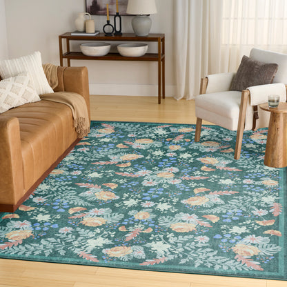Teal floral area rug on light wood floor with tan leather sofa, white armchair, and wooden console in a bright living room.