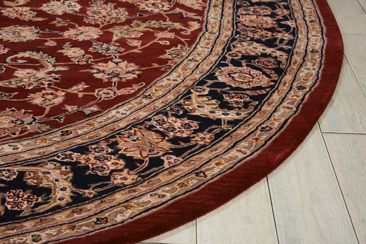Round oriental rug with red field, navy floral border, and ivory outer edge on light tile floor.