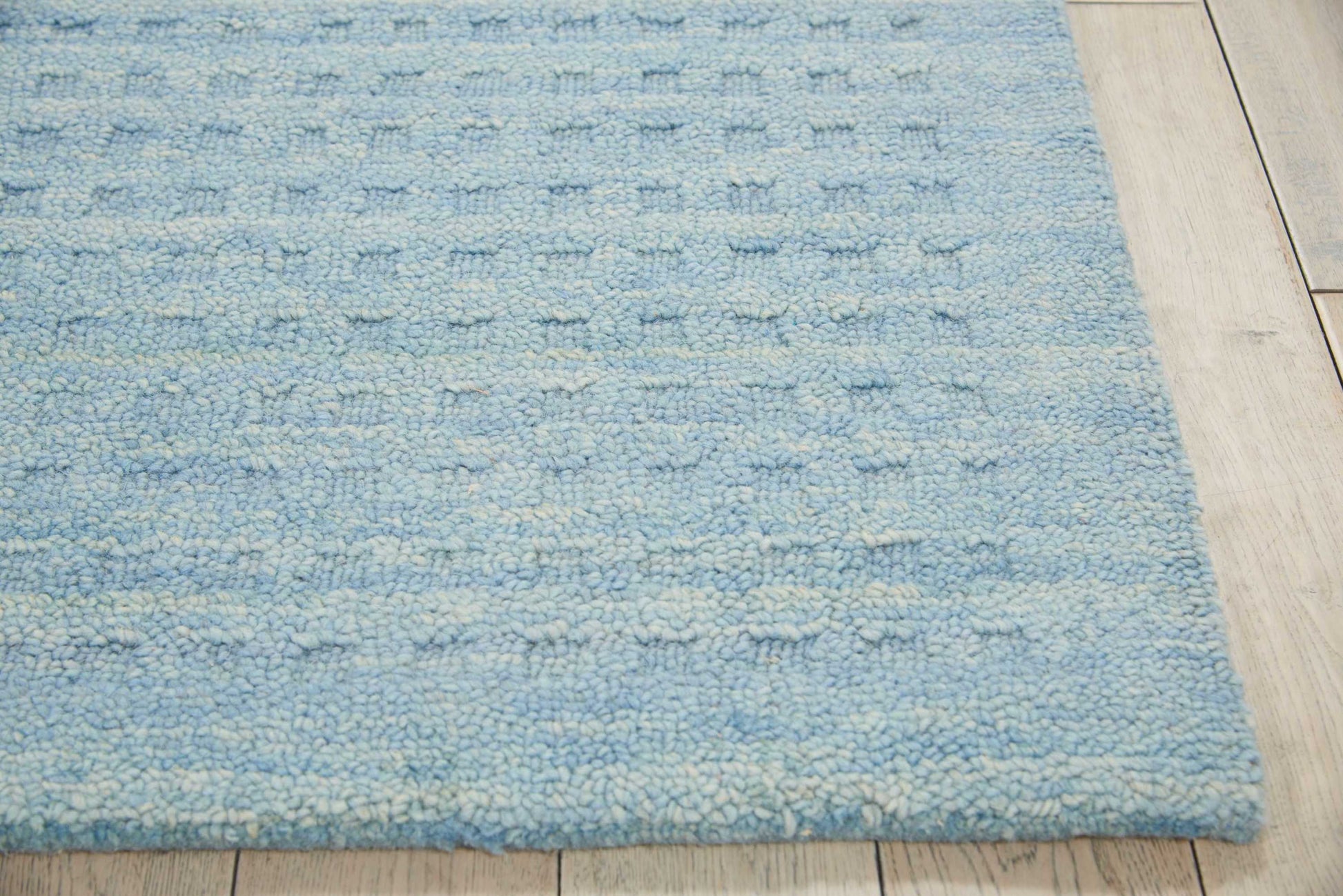 Blue loop-pile area rug with pale cream flecks on a light wood floor.